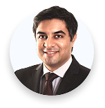 Portrait of a man in a dark suit and tie smiling against a white background.