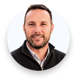 Smiling man with short dark hair and beard wearing a black jacket and white shirt.