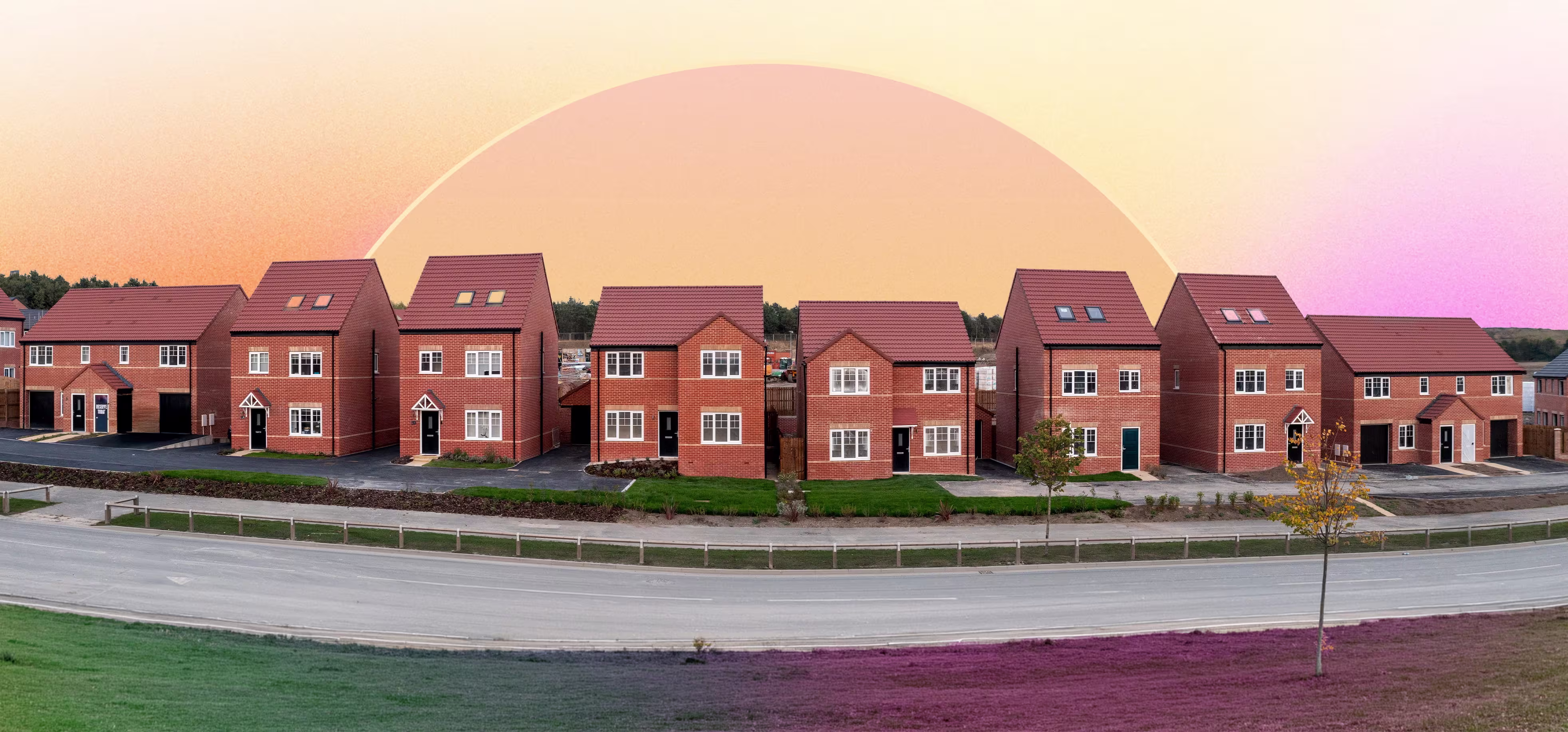 A row of seven modern two-story brick houses with pitched roofs along a curved road, under a sunset sky with a large pale sun near the horizon.