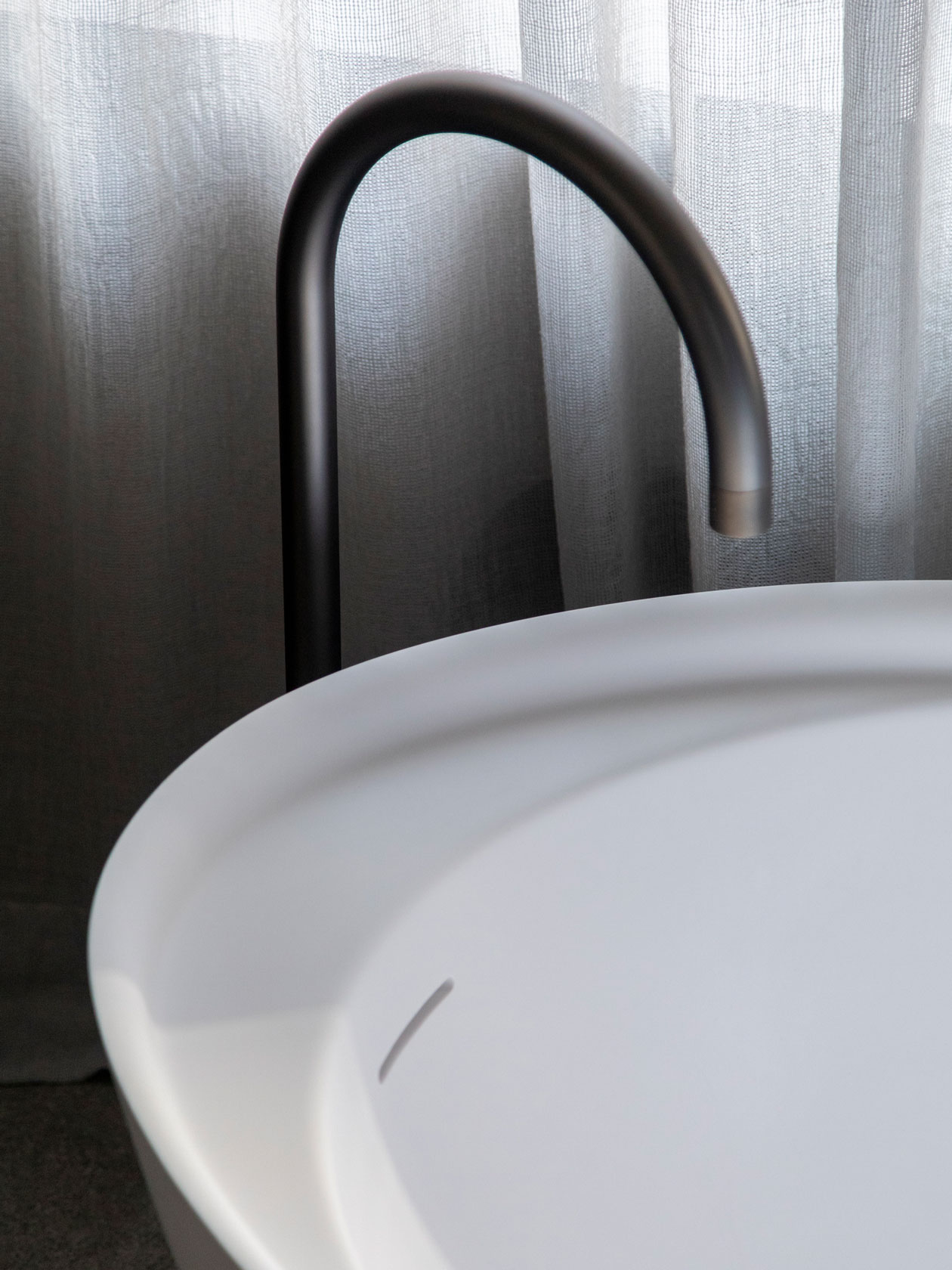 Detail of a white basin with a dark curved tap