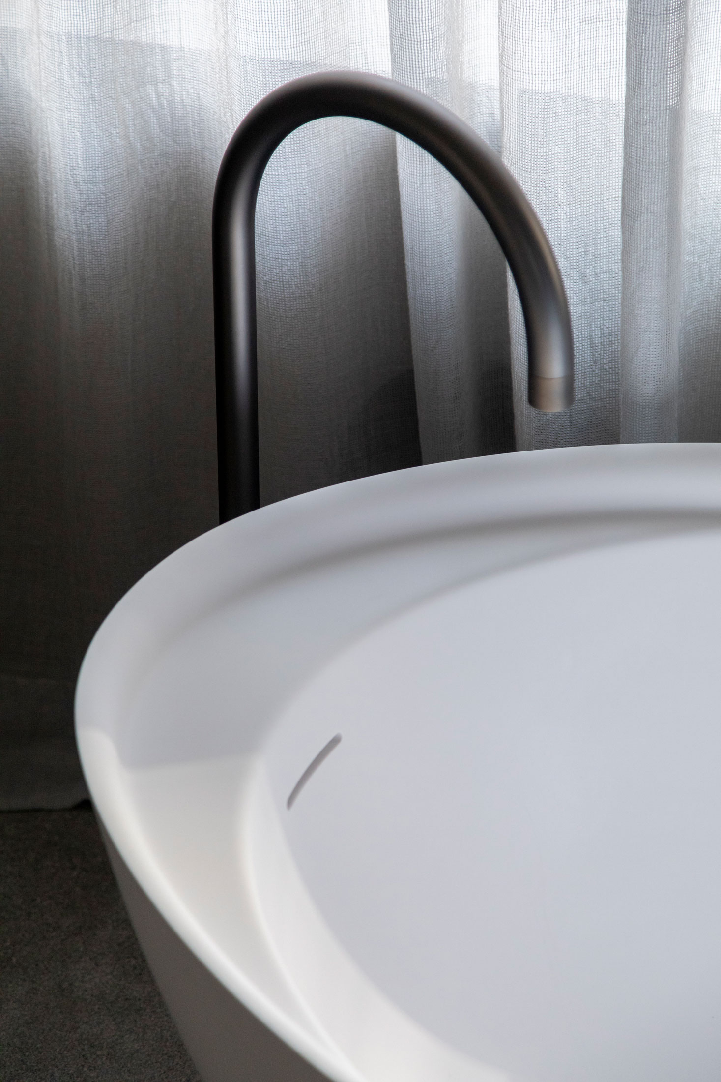 White basin and dark tap in front of a light curtain