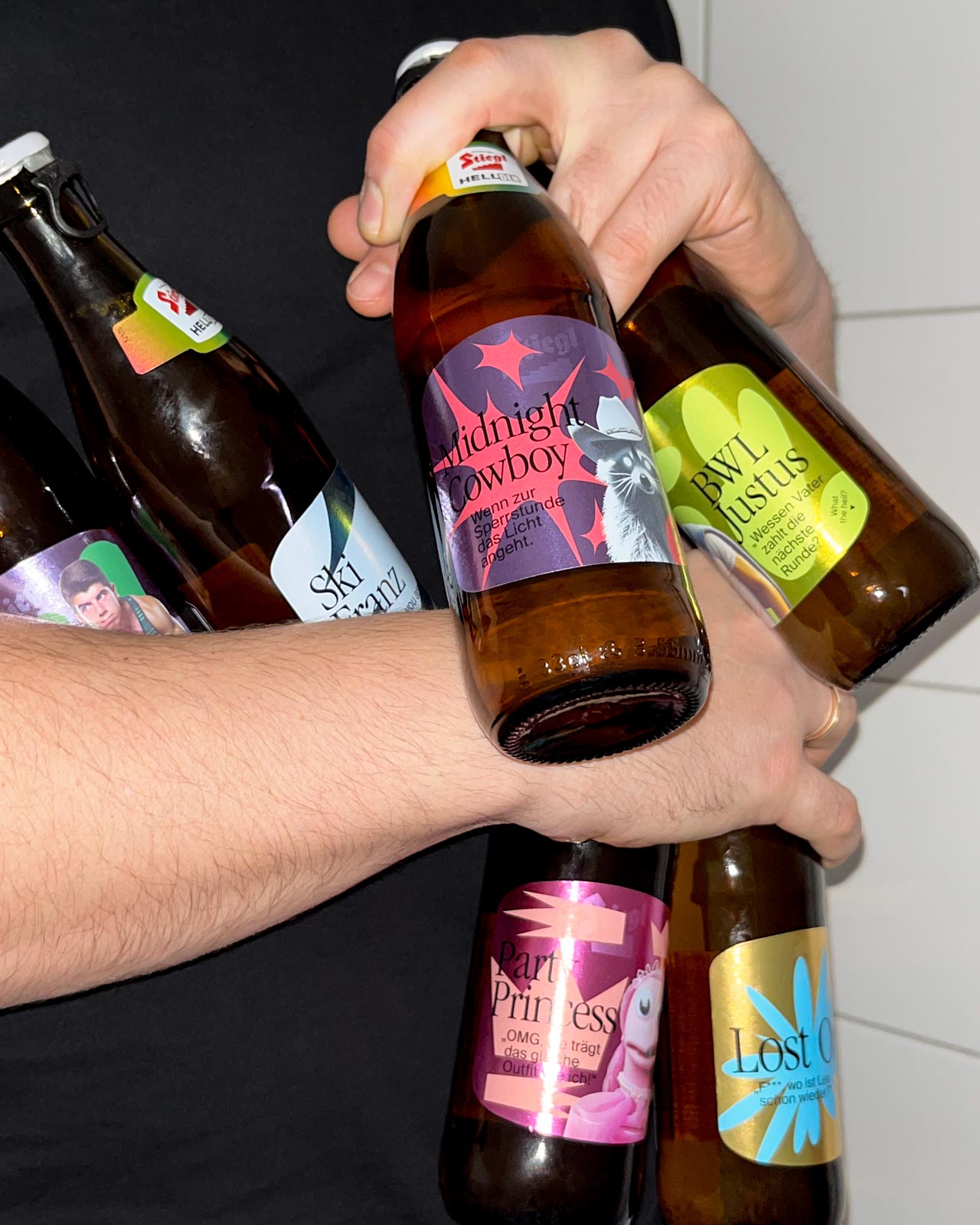 Hände stoßen mit Stiegl-Bierflaschen mit bunten Sonderetiketten an