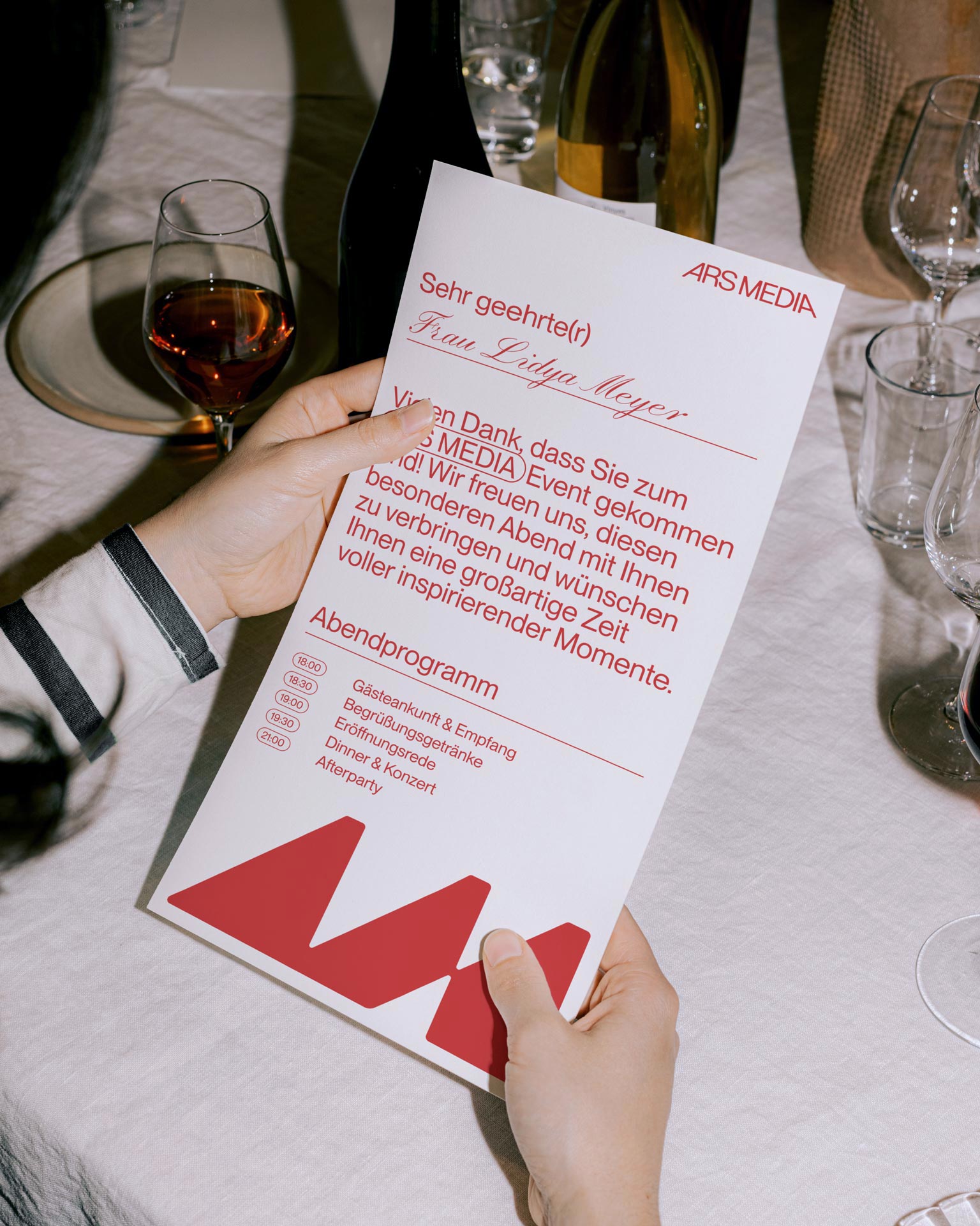 White Ars Media menu or programme card with a red symbol at a set table