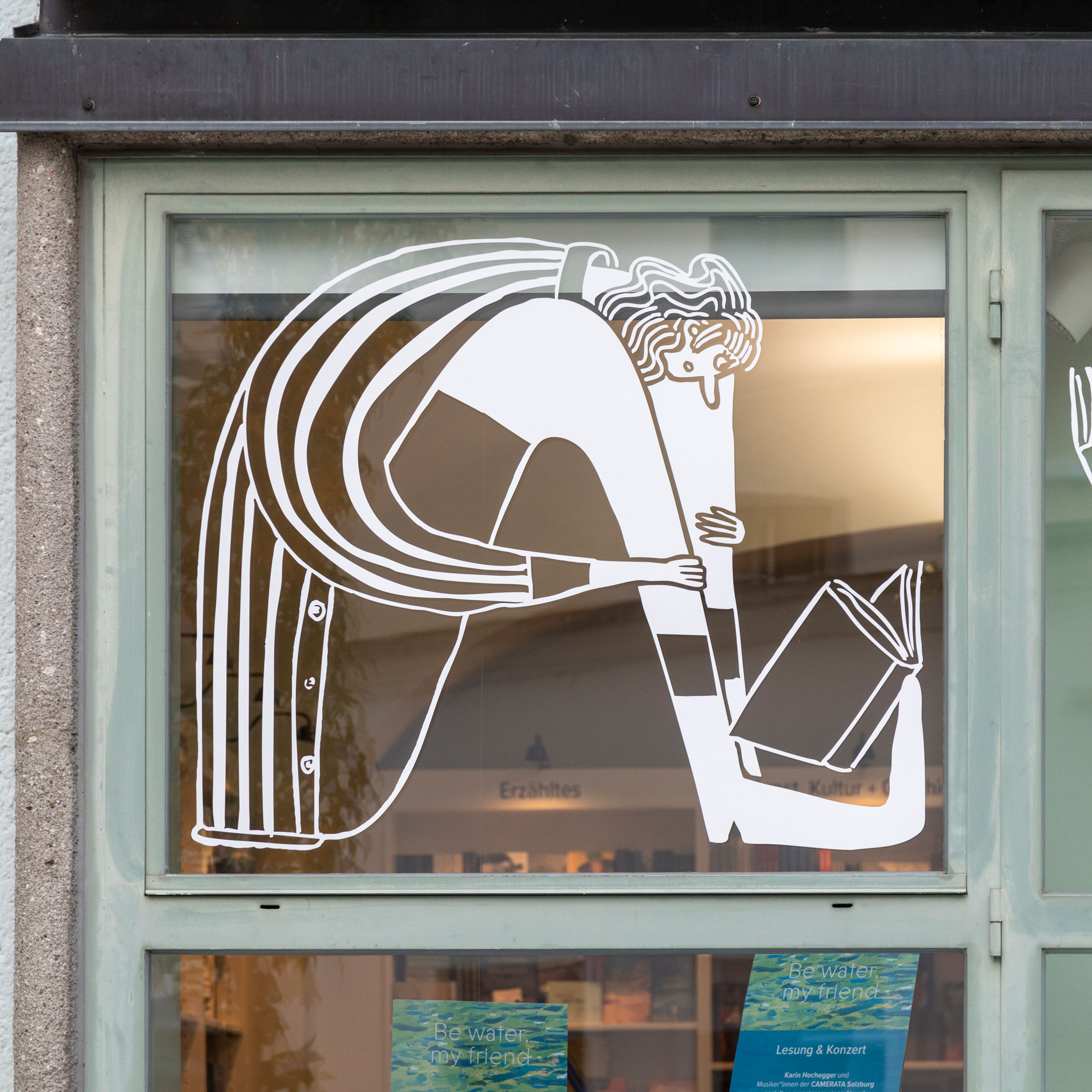 Window illustration of a bent figure with long hair and an open book