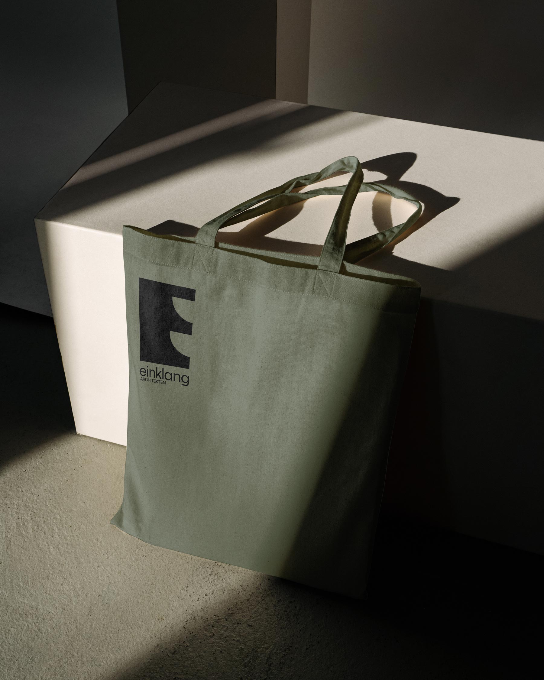 Green tote bag with a black Einklang symbol beside a pale plinth