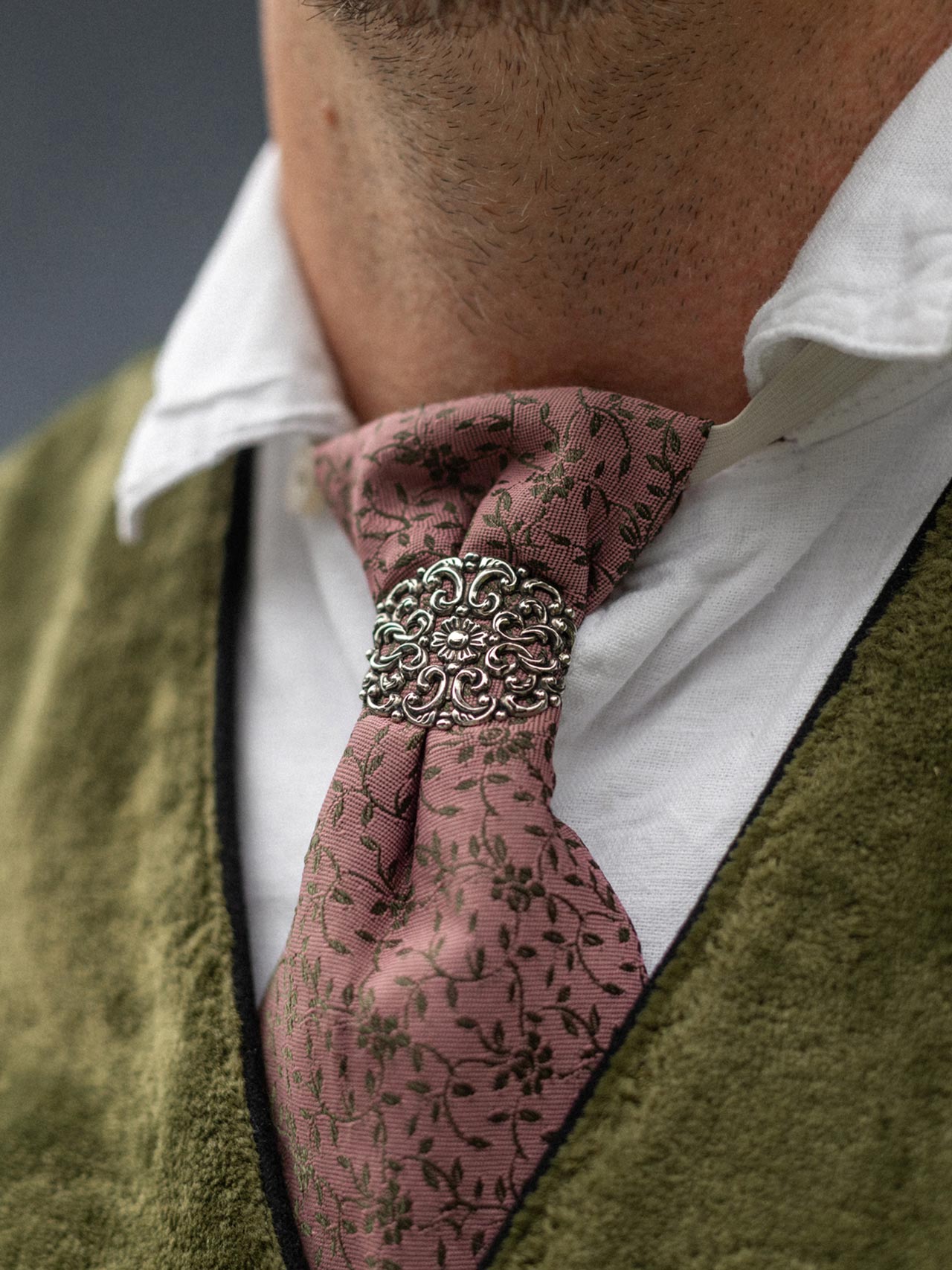 Close-up of a traditional tie with a decorative clasp and green waistcoat