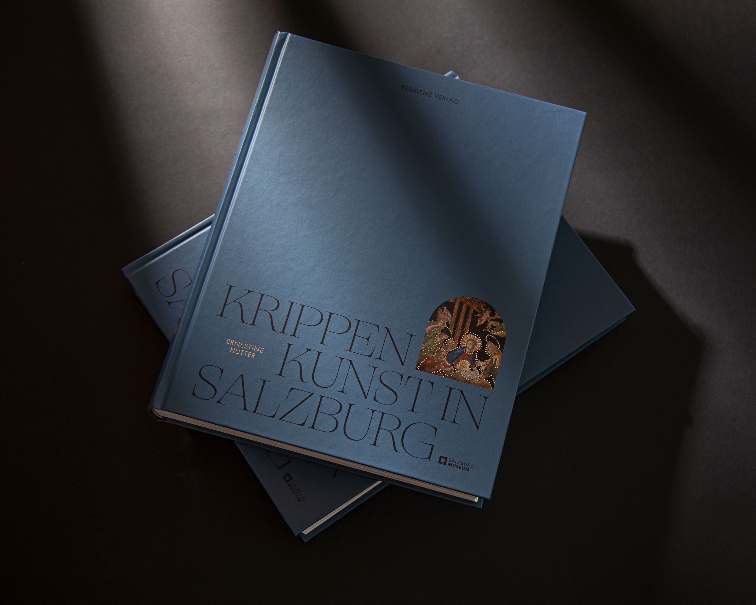 Stacked dark blue Krippenkunst in Salzburg books with an inset cover image