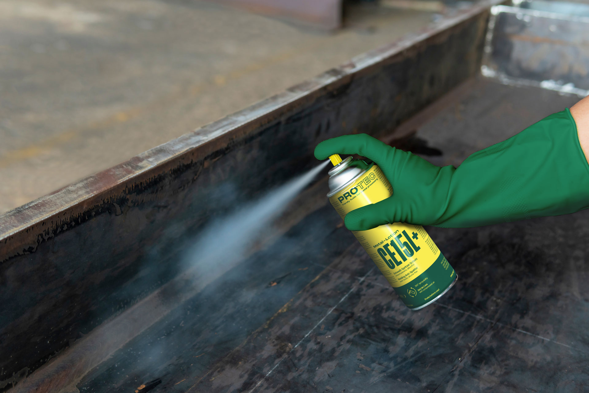 Hand in a green protective glove applying a PROTEC spray to metal