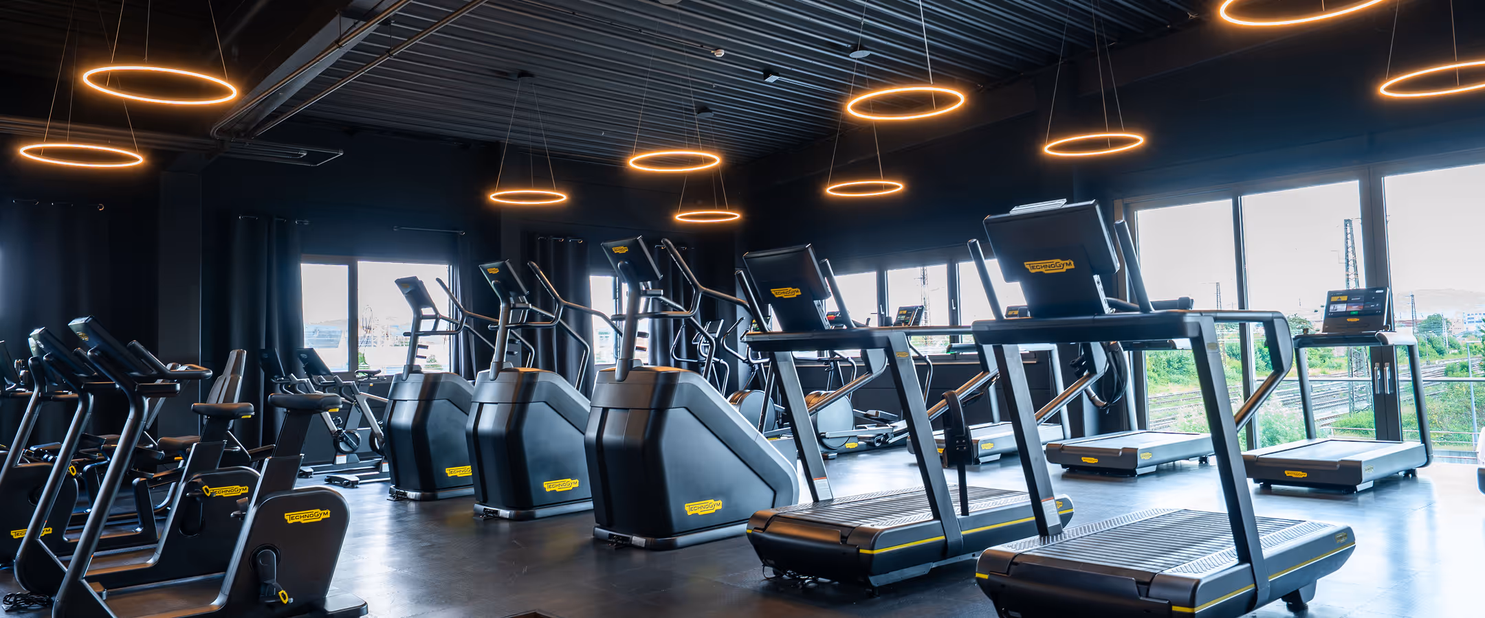Modern gym with cardio machines including treadmills and ellipticals under glowing ring lights.