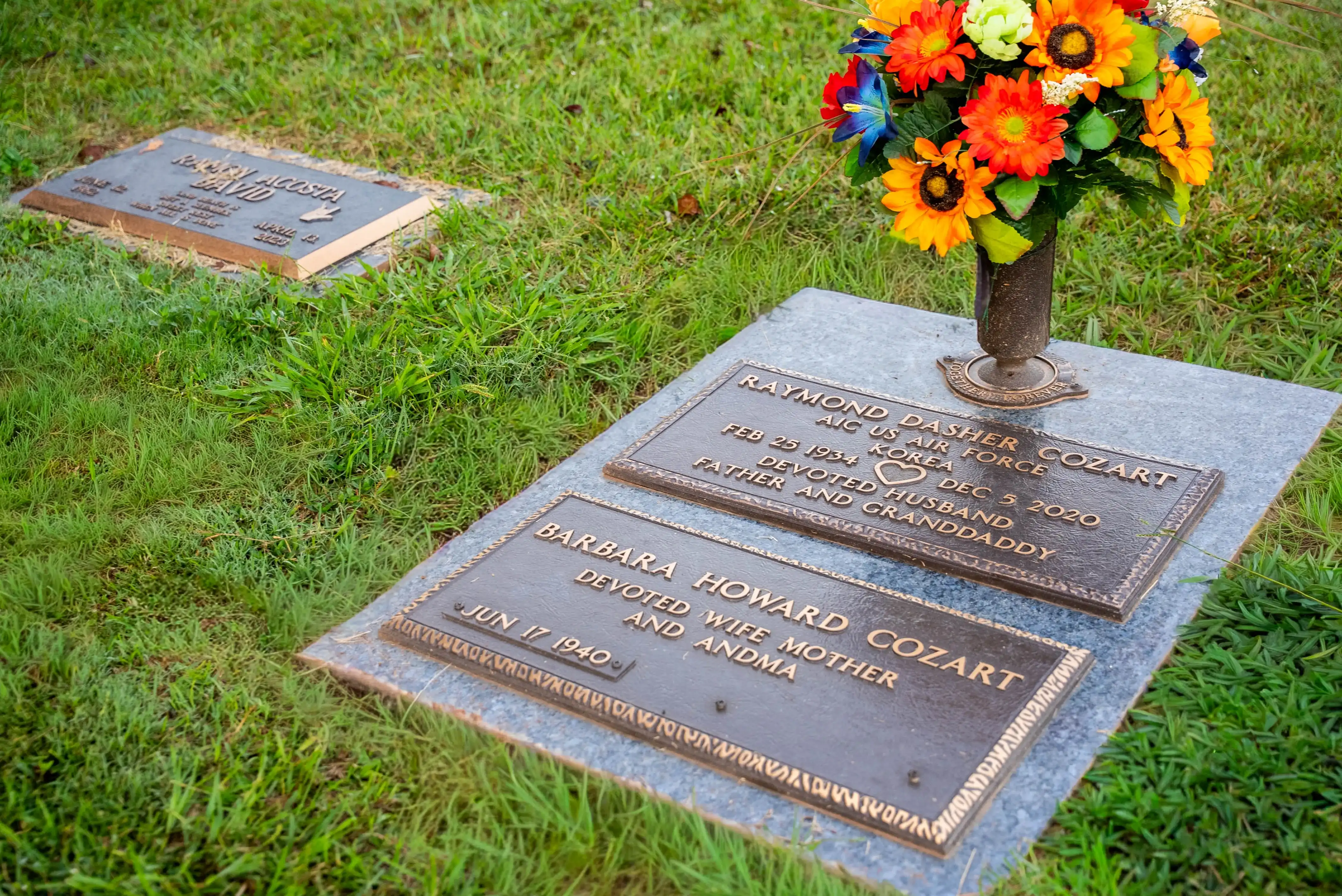 Bronze companion markers for a husband and wife on a granite base with a vase of bright flowers