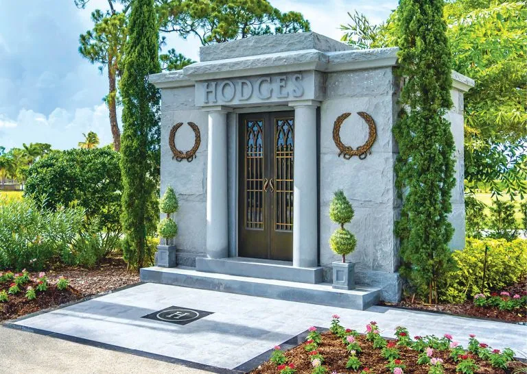 White granite walk-in mausoleum with columns, bronze doors and landscaped garden