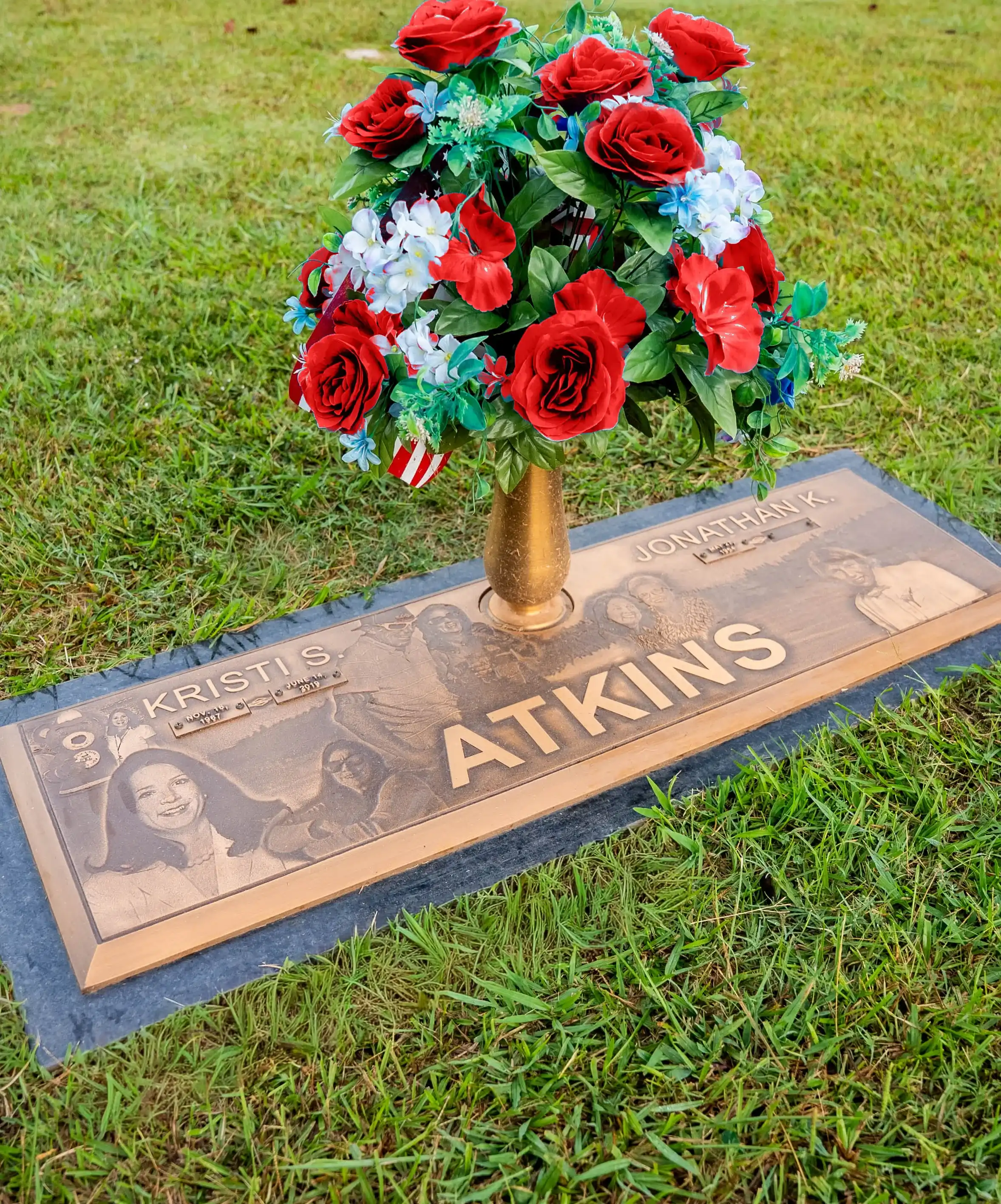 Bronze companion marker with etched family portraits and a vase of red and white roses