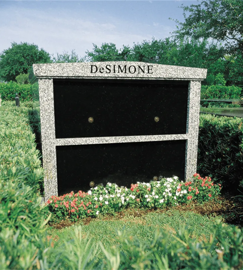Granite private family mausoleum with two black crypt fronts and flowers planted at the base