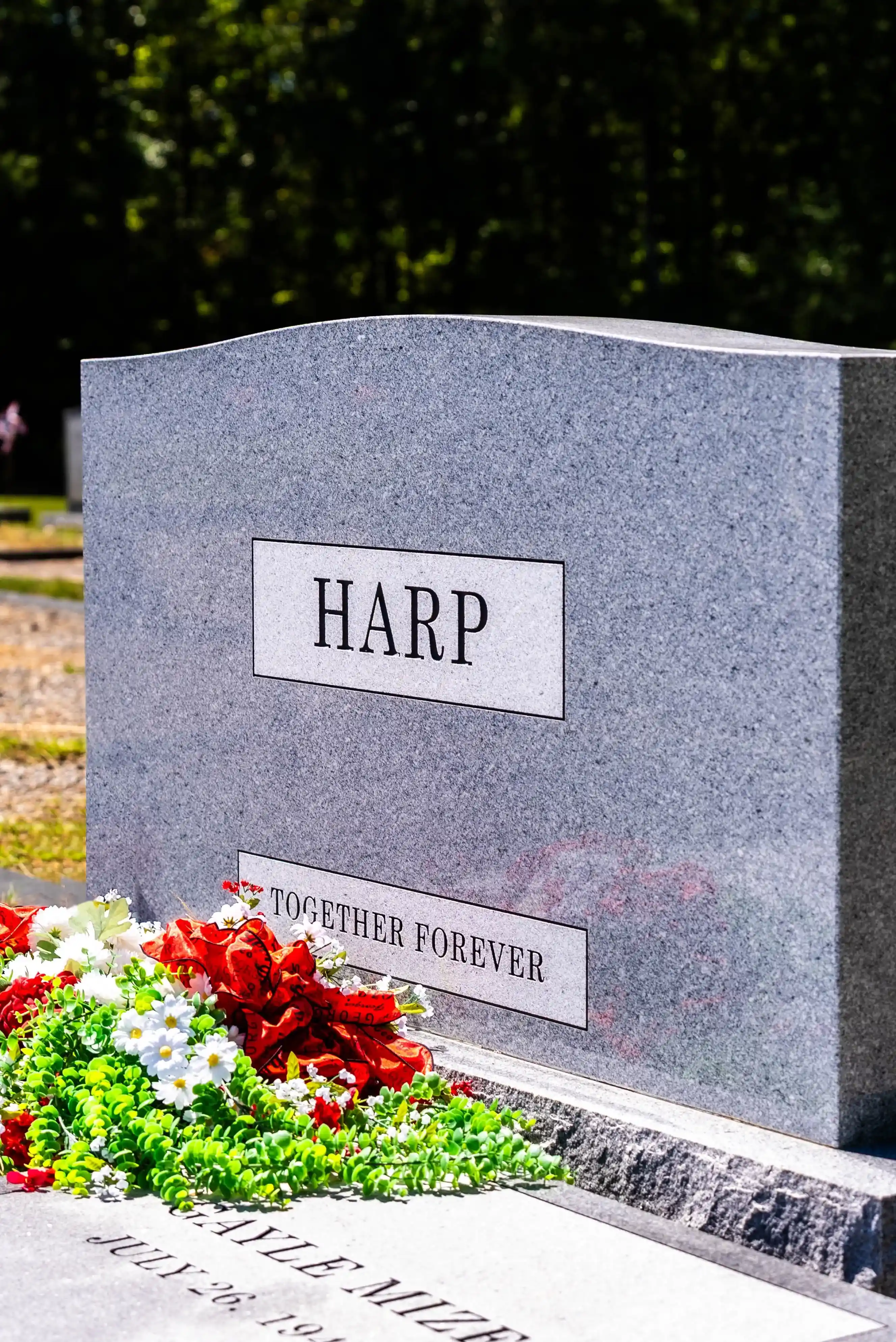 Gray granite upright headstone with a polished name panel and red and white flowers at the base