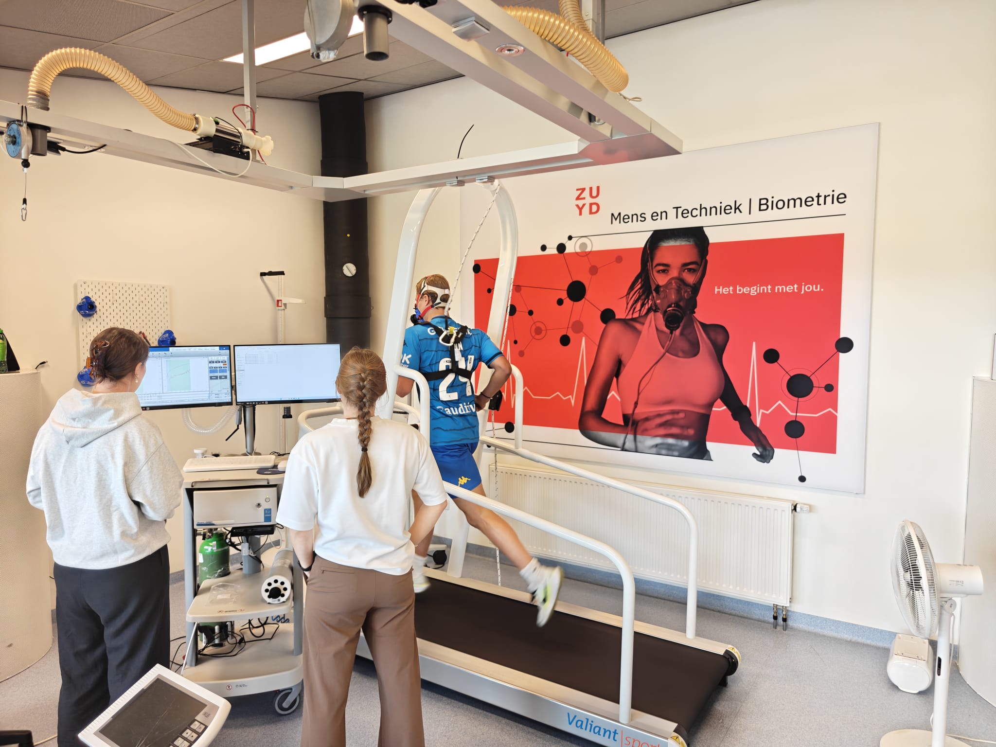 Man rennend op loopband met ademhalingsmasker in een laboratorium met twee toezichthouders.