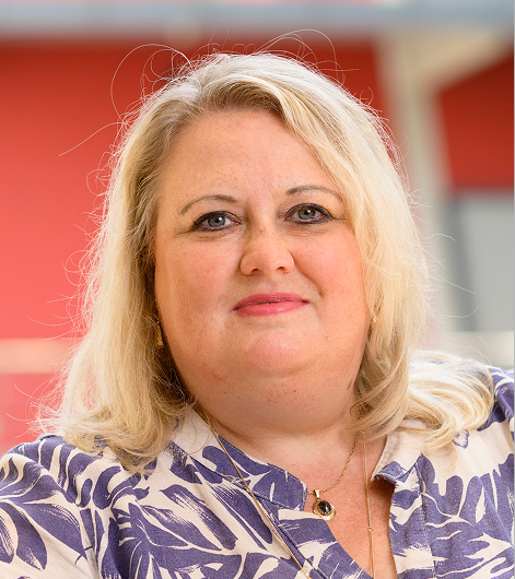 Portret van een vrouw met blond haar en een blouse met paars-wit patroon voor een rode achtergrond.
