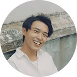 Homme souriant avec une chemise blanche assis devant un mur gris.