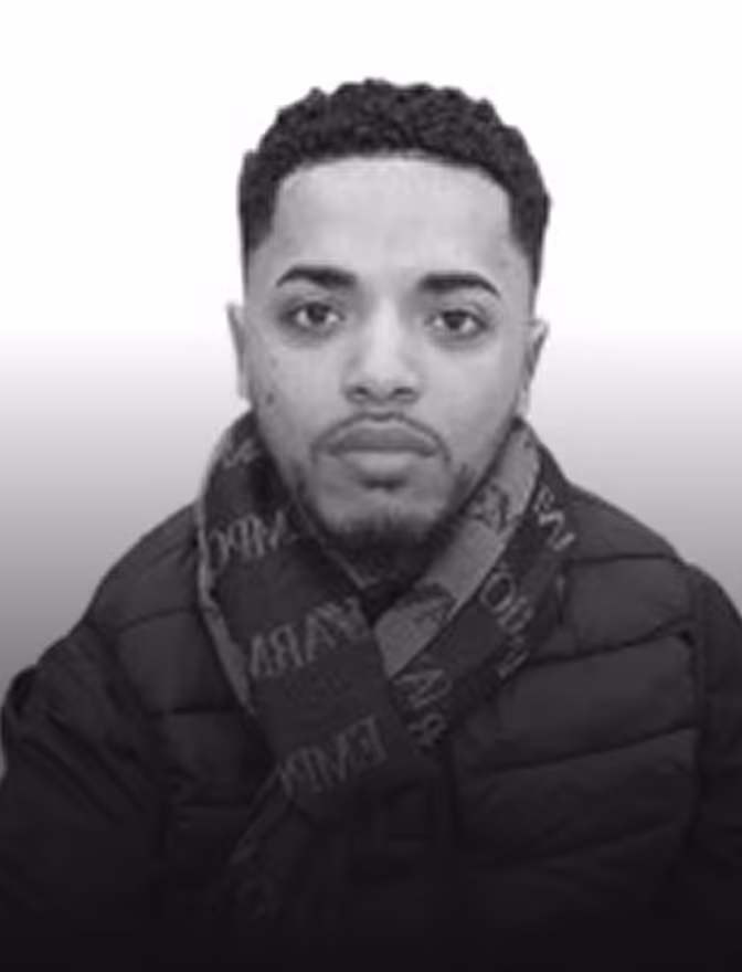 Portrait en noir et blanc d'un homme avec une barbe courte, écharpe et veste matelassée.