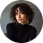 Portrait d'une femme aux cheveux bouclés et visage sérieux portant un pull noir.