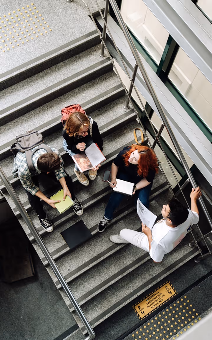 Quatre étudiants assis sur des escaliers discutant avec des livres et cahiers.
