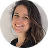 Portrait d'une femme souriante aux cheveux longs et foncés sur fond clair.