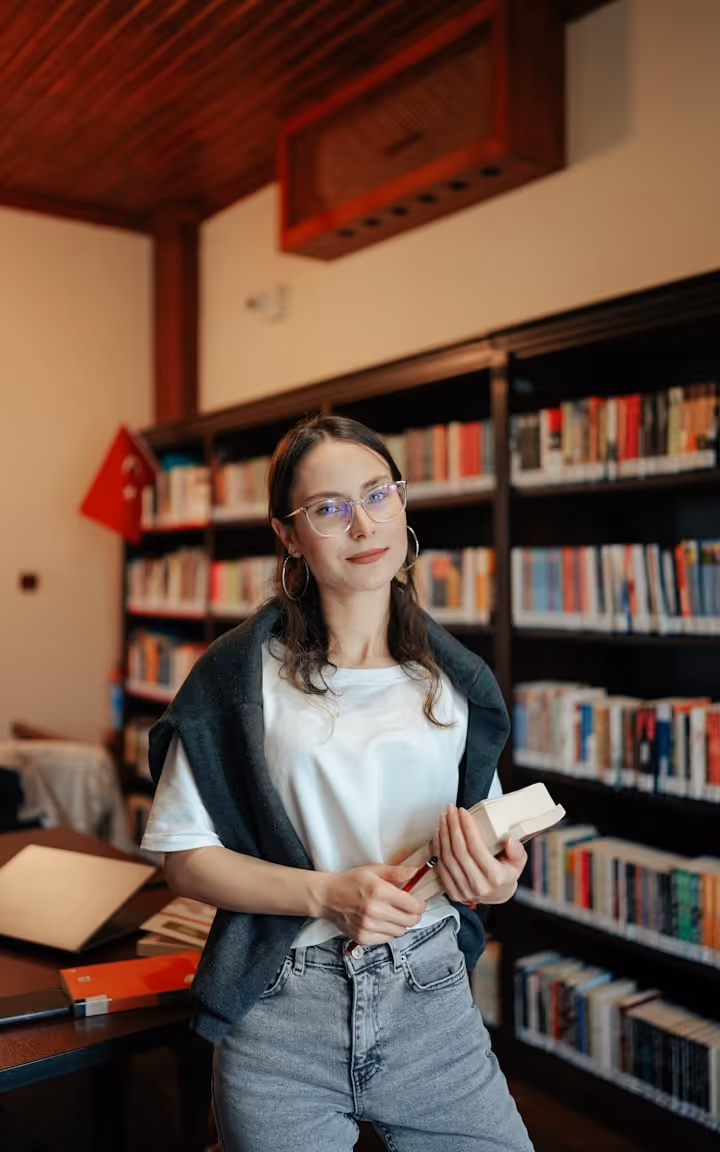 Jeune femme avec lunettes tenant un livre dans une bibliothèque moderne avec des étagères remplies