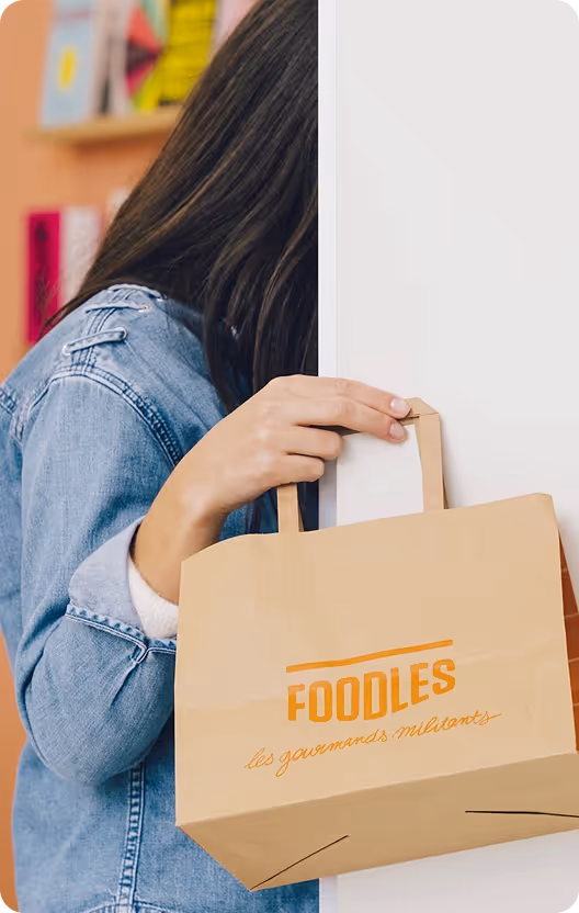 Personne tenant un sac en papier Foodles à côté d’une porte blanche.