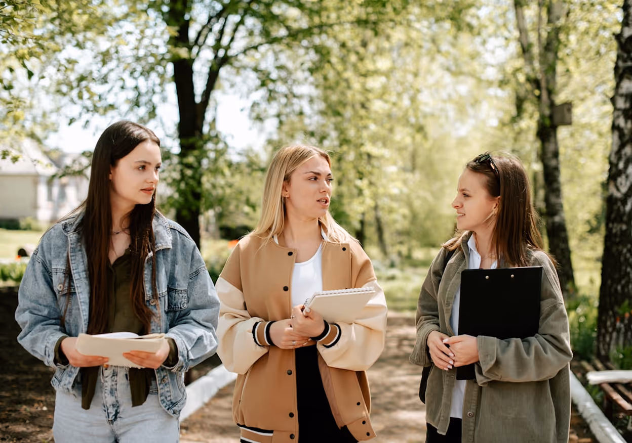 Trois étudiantes marchant et discutant dans un parc avec des notes et un classeur.