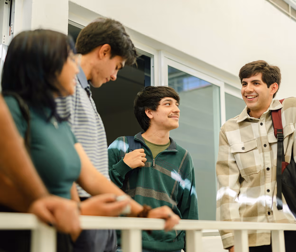 Groupe de jeunes étudiants souriants discutant dehors près d'une fenêtre.