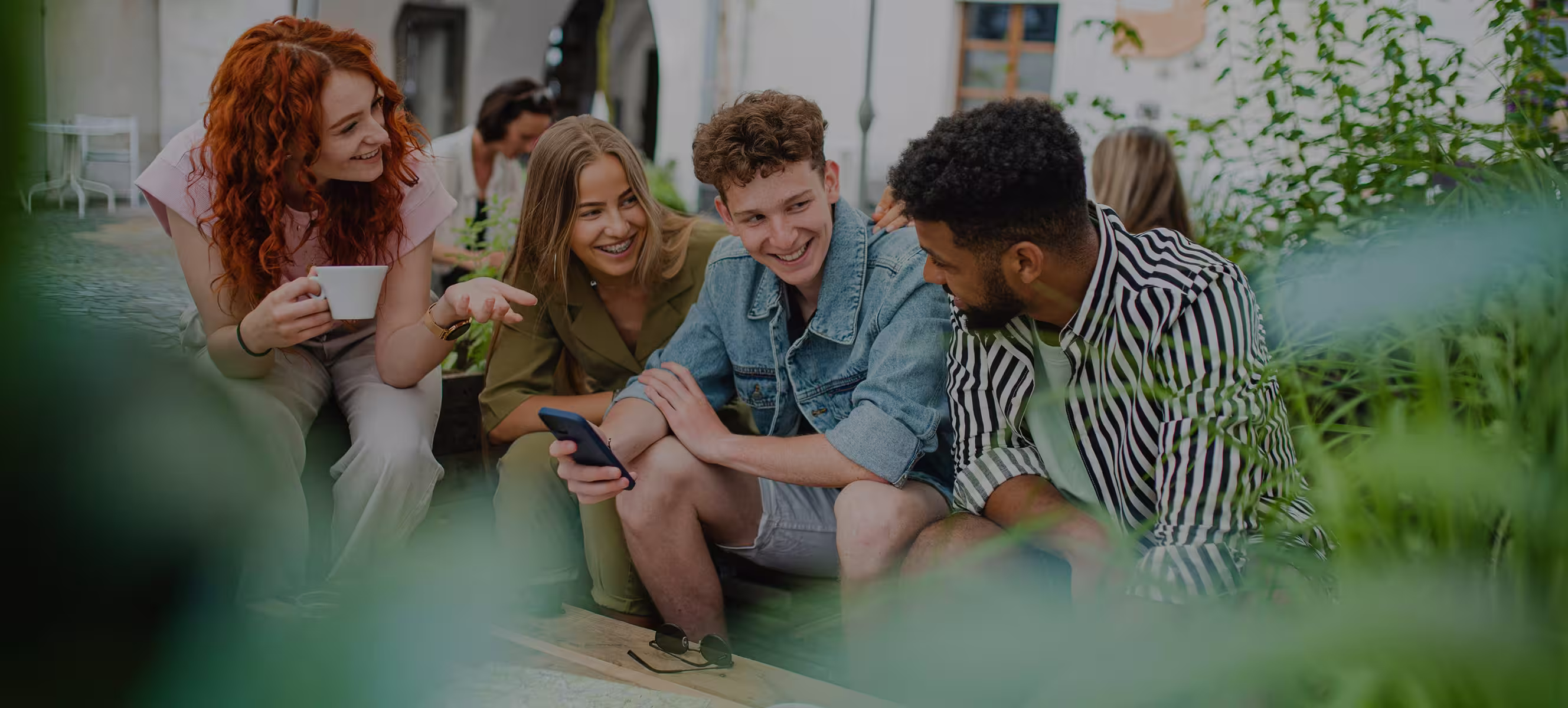Groupe d'amis souriants assis à l'extérieur, une personne montre un téléphone portable.