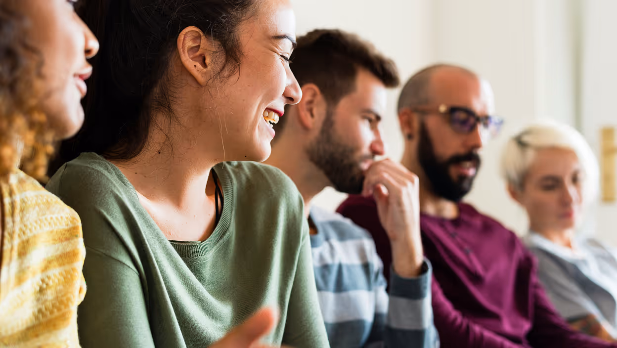 Groupe de personnes assises en rangée, souriante et discutant dans un environnement lumineux.