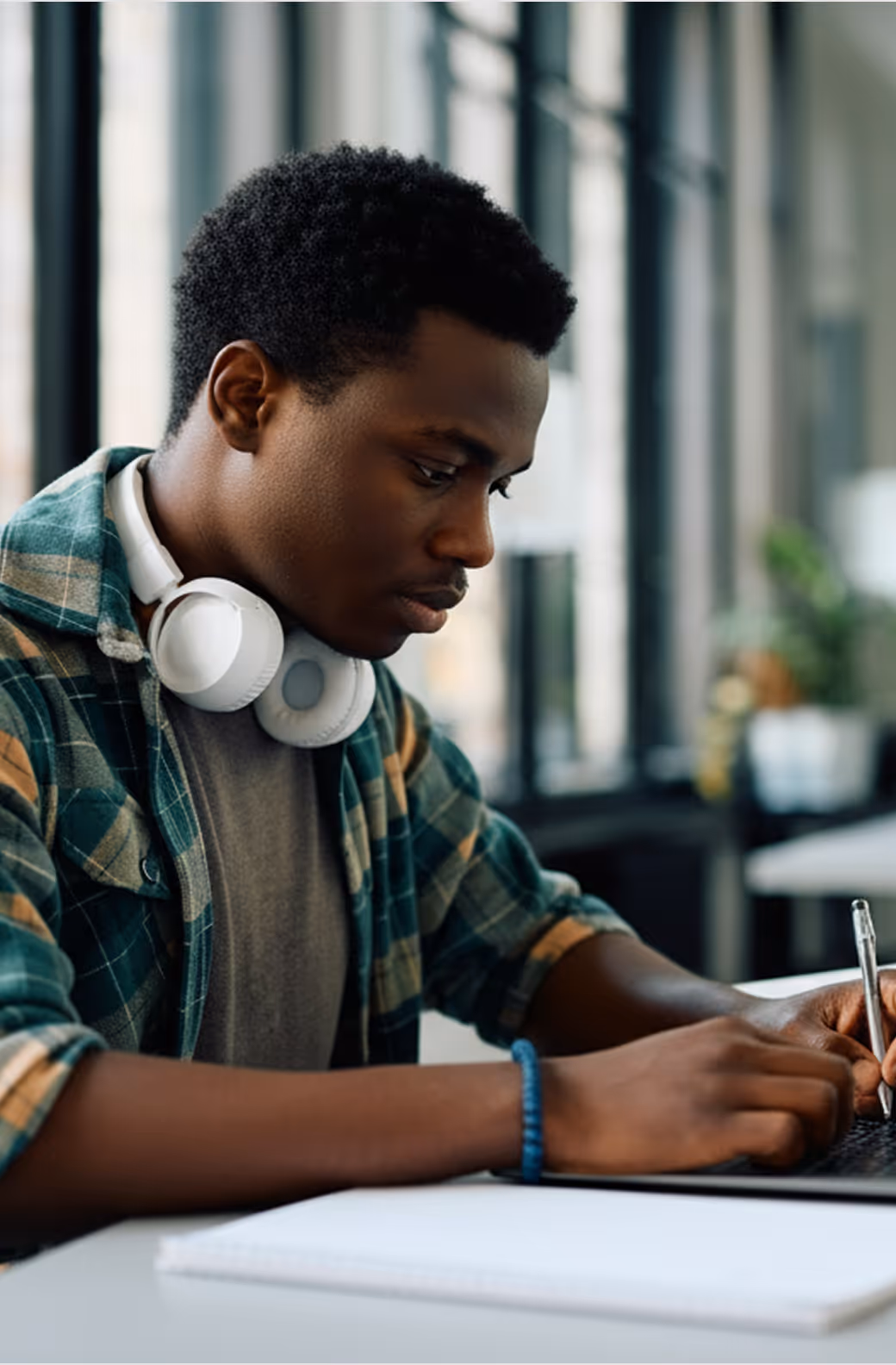 Jeune homme portant un casque blanc écrivant avec un stylo dans un cahier dans un bureau lumineux.
