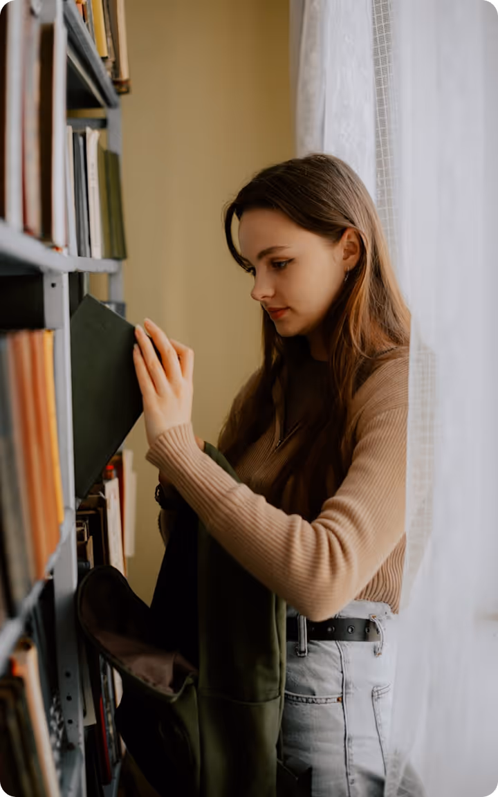 Jeune femme choisissant un livre sur une étagère dans une bibliothèque lumineuse près d'une fenêtre.
