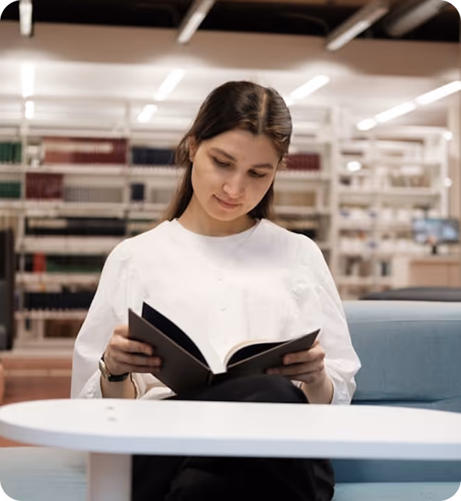 Une femme assise lisant un livre dans une bibliothèque moderne et lumineuse.