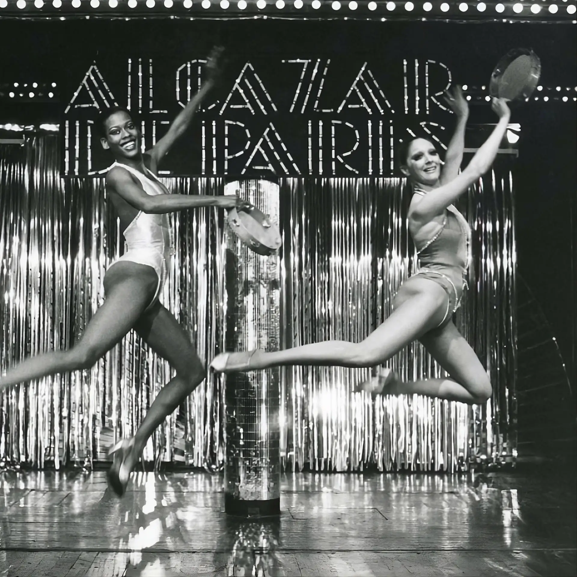 Deux danseuses sautant sur scène devant l'enseigne lumineuse Alcazar de Paris, photographie vintage en noir et blanc