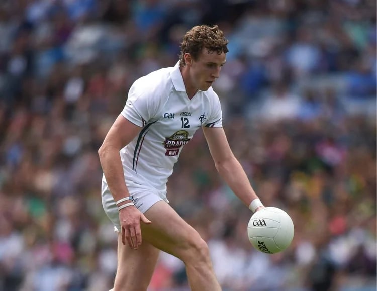 Male Gaelic football player in white jersey controlling a white ball during a match.