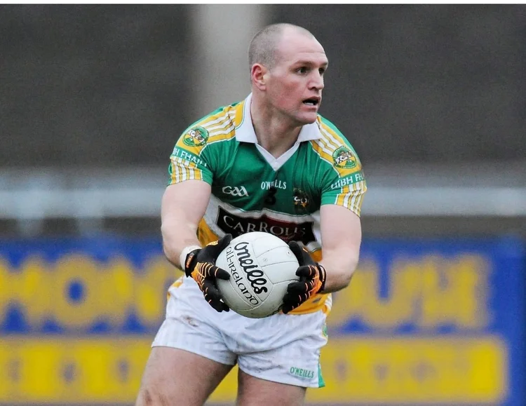 Gaelic football player in green and yellow jersey holding a white O'Neills ball preparing to pass.