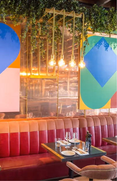 Red and pink velvet banquette beneath bold geometric wall panels and brass pendant lights at Angelina's
