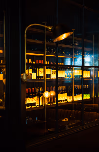 Backlit wine shelves and a brass lamp above banquette seating in the dark dining room at Doolally
