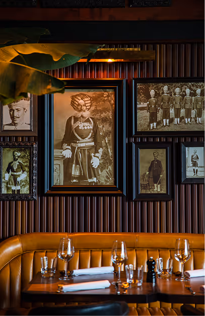 Tan leather banquette and a set table beneath framed sepia portraits in the dining room at Doolally