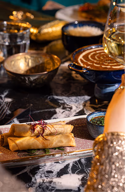 Crispy rolls, curry and rice in brass and blue dishes on a marble table at Doolally