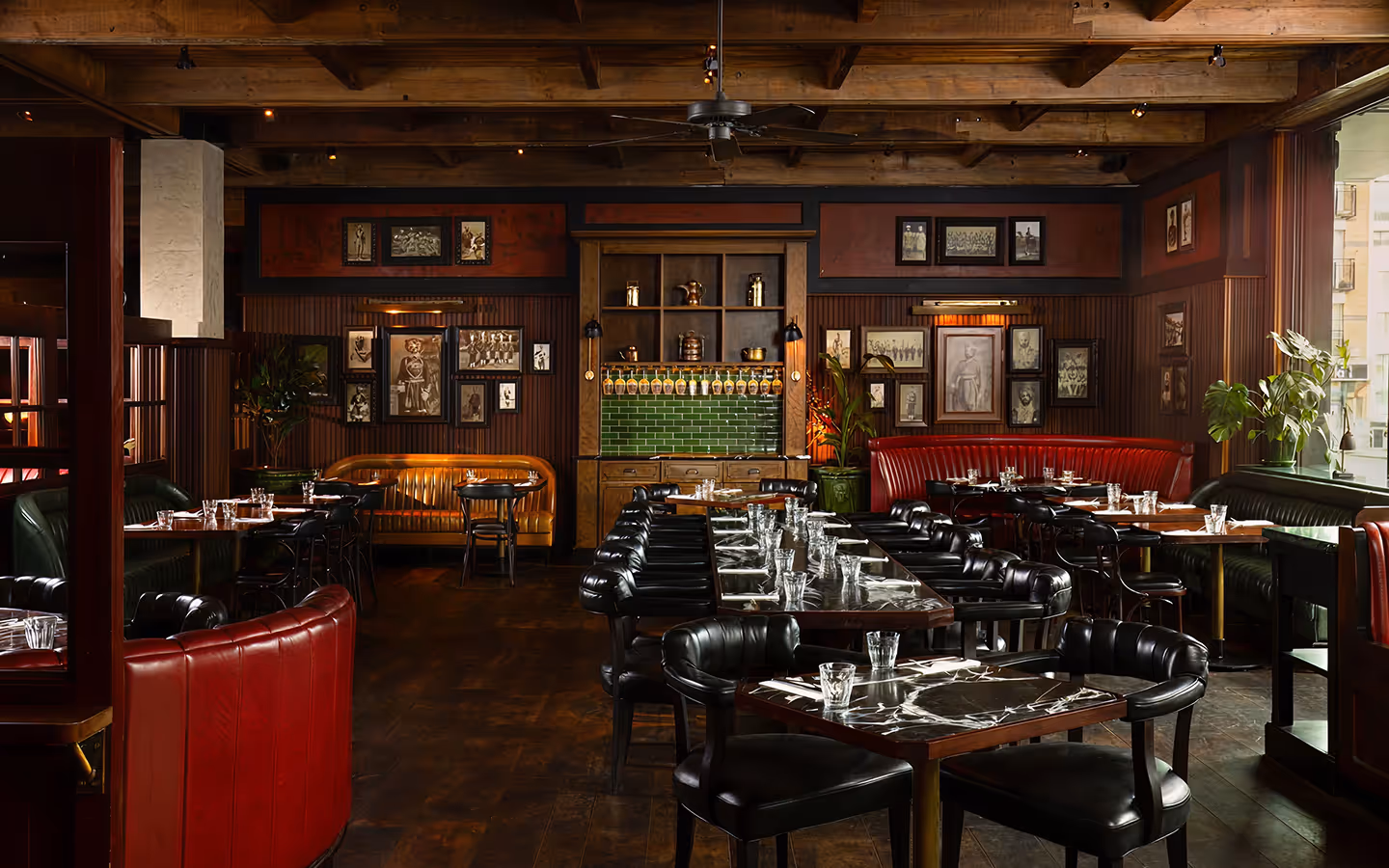 Dining room with red leather banquettes, marble tables and a gallery wall of framed portraits at Doolally