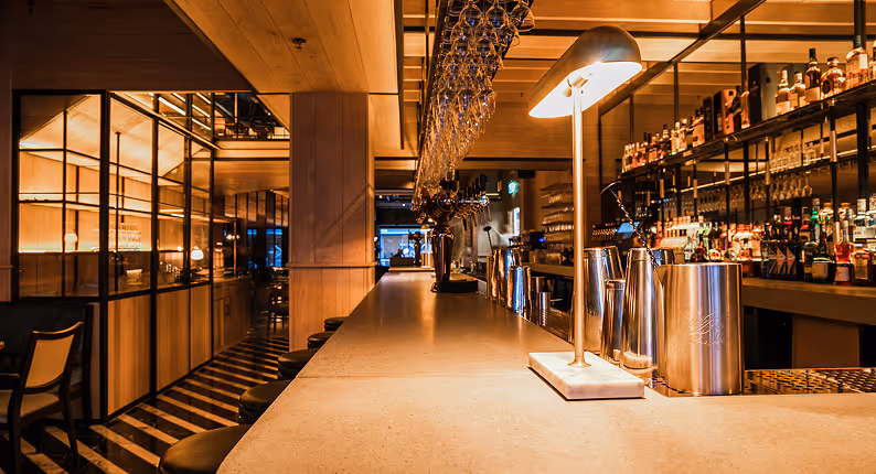 Pale stone bar counter with hanging glassware and a wall of spirits