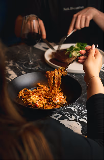 Diners sharing pasta and steak with a glass of red wine at a marble table in Isabelle's