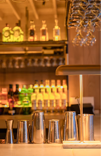 Cocktail shakers and a brass lamp on the bar top beneath hanging glassware at Isabelle's