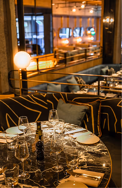 Marble table set with wine glasses beside patterned banquettes and brass rails at Isabelle's