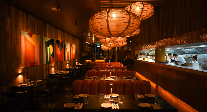 Woven rattan pendants over terracotta banquettes beside the open kitchen at Kaldero