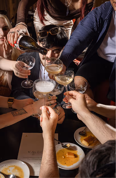 Group toasting with coupes of sparkling wine over dessert plates at Kaldero