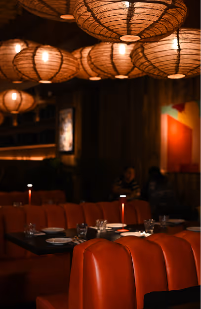 Woven globe lanterns above orange leather banquettes and candlelit tables at Kaldero