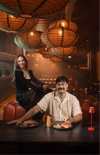 Two guests at a table of crab dishes beneath woven lanterns at Kaldero